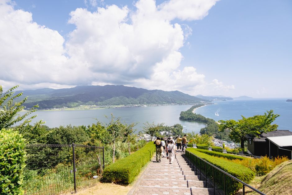 遊客沿階梯步道走下瞭望台，遠眺天橋立沙洲與宮津灣海景