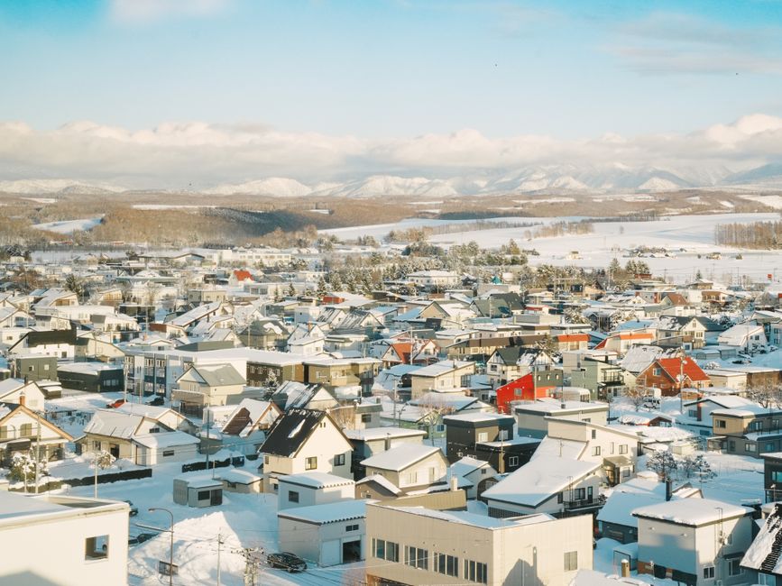 雪後北海道小鎮空拍景象，屋頂覆滿白雪、遠山環繞