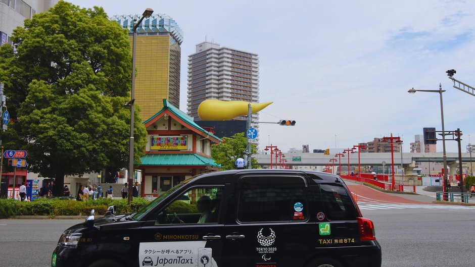 日本交通的黑色計程車駛過東京街頭，背景是朝日啤酒大樓與金色火焰造型地標